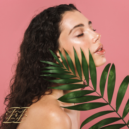 Close-up of a woman with radiant, glowing skin and long brown hair, holding a green leaf, symbolizing the natural nourishment and rejuvenation provided by Feliz Faces Cosmetics skincare products.